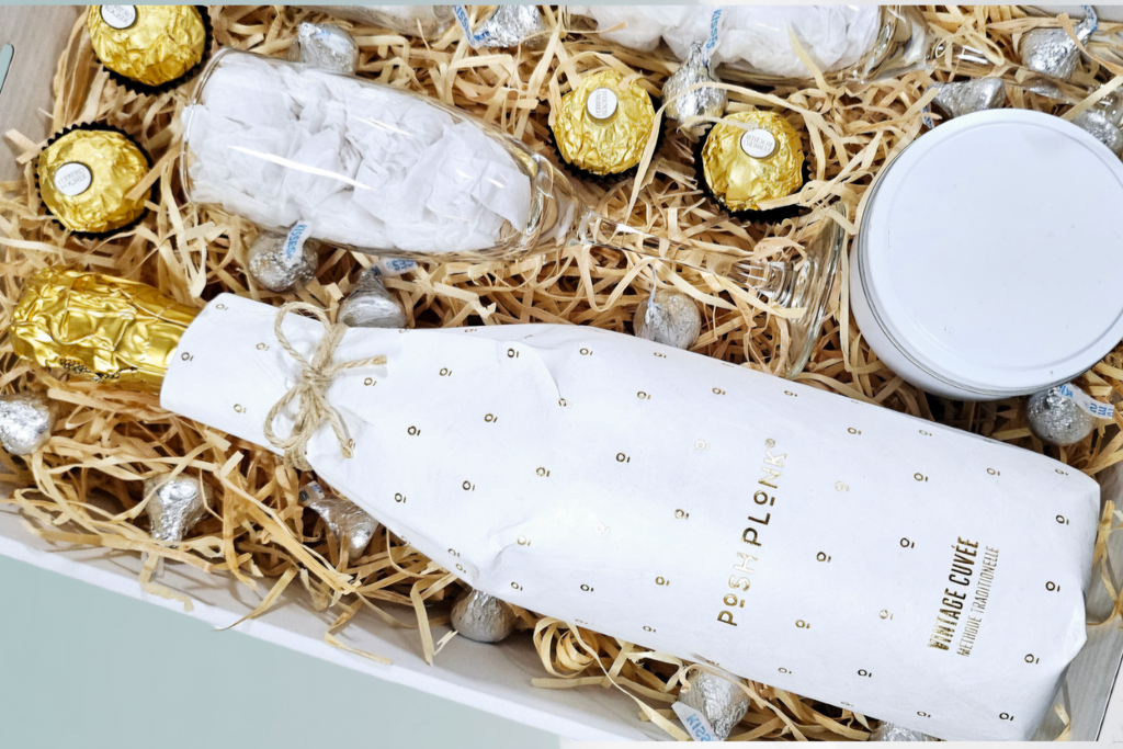 Posh Plonk Vintage Cuvee Sparkling Gift Box: The ultimate relaxation gift featuring a 750ml bottle of Posh Plonk Shiraz, Candle Queens Bath Soak, a 200g scented candle, Ferrero Rocher chocolates, Hershey's Kisses, and two elegant wine glasses. Adorned with signature confetti, a beautiful bow, and a personalized message card for the perfect indulgent gift.