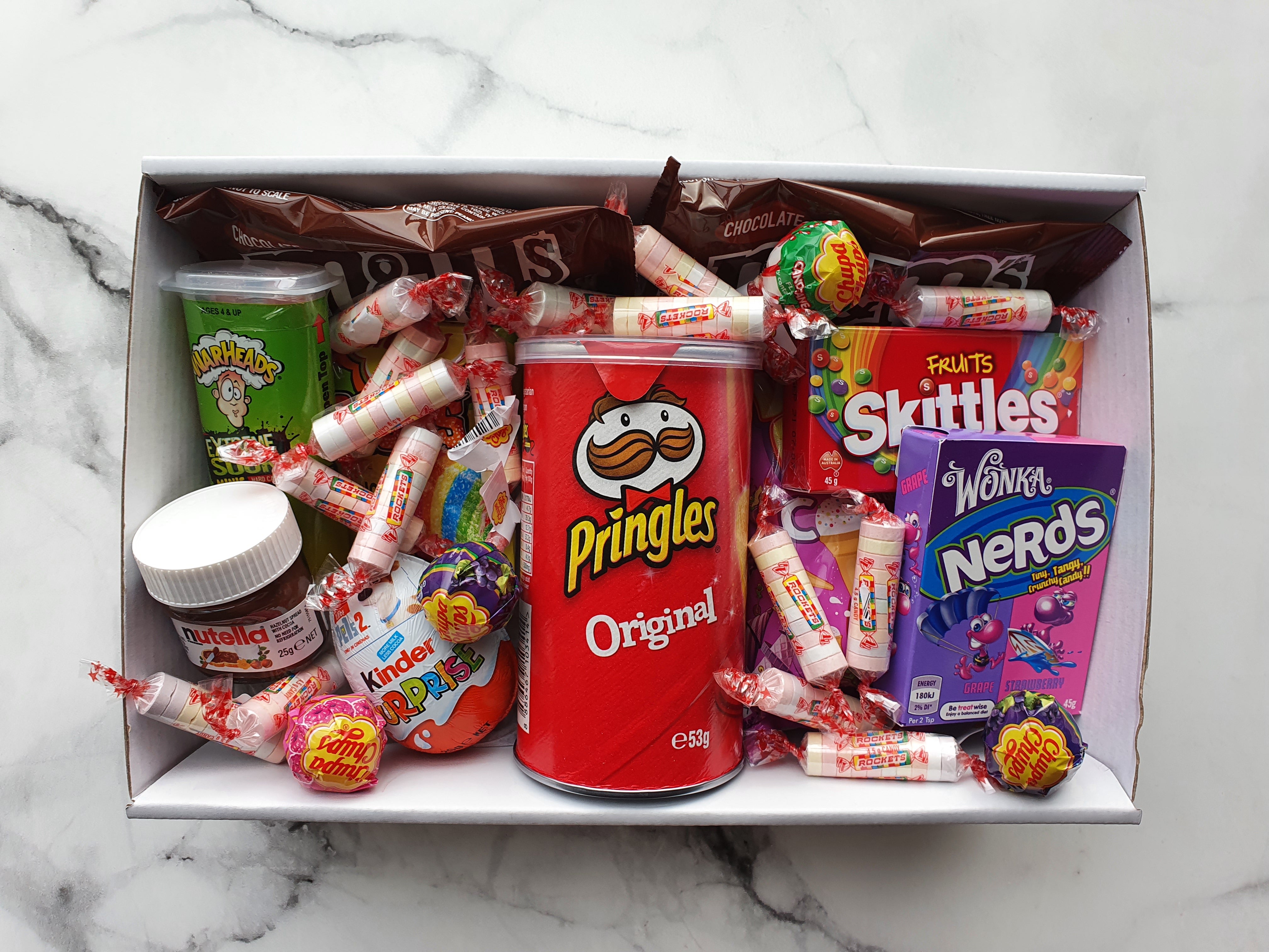 Mini Treats Package: A fun assortment of sweet snacks including a Mini Pringles pack, Nerds box, Skittles packet, Kinder Surprise egg, 4 Chupa Chups lollipops, mini wrapped chocolates, a mini Nutella jar, and assorted lollies, sours, or chocolates. Packaged in a 255 x 155 x 80 mm box, perfect for indulgence or gifting.