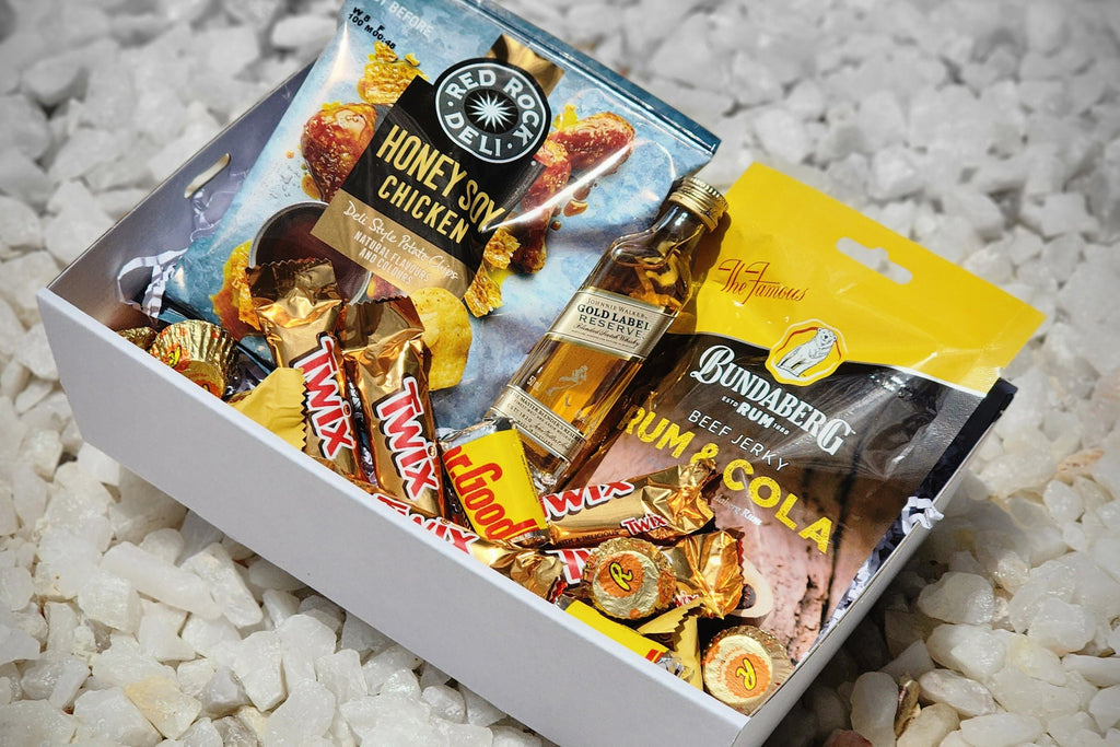 Gold Label Johnnie Walker Mini & Treats: The perfect small gift for scotch lovers. Includes 50ml Gold Label Johnnie Walker, Red Rock Deli Honey Soy Chips, Dr Proctor’s Beef Jerky, Mini Twix, Hershey’s, Reese’s Peanut Butter Cups, and Toblerone chocolates, all elegantly packed in a gift box