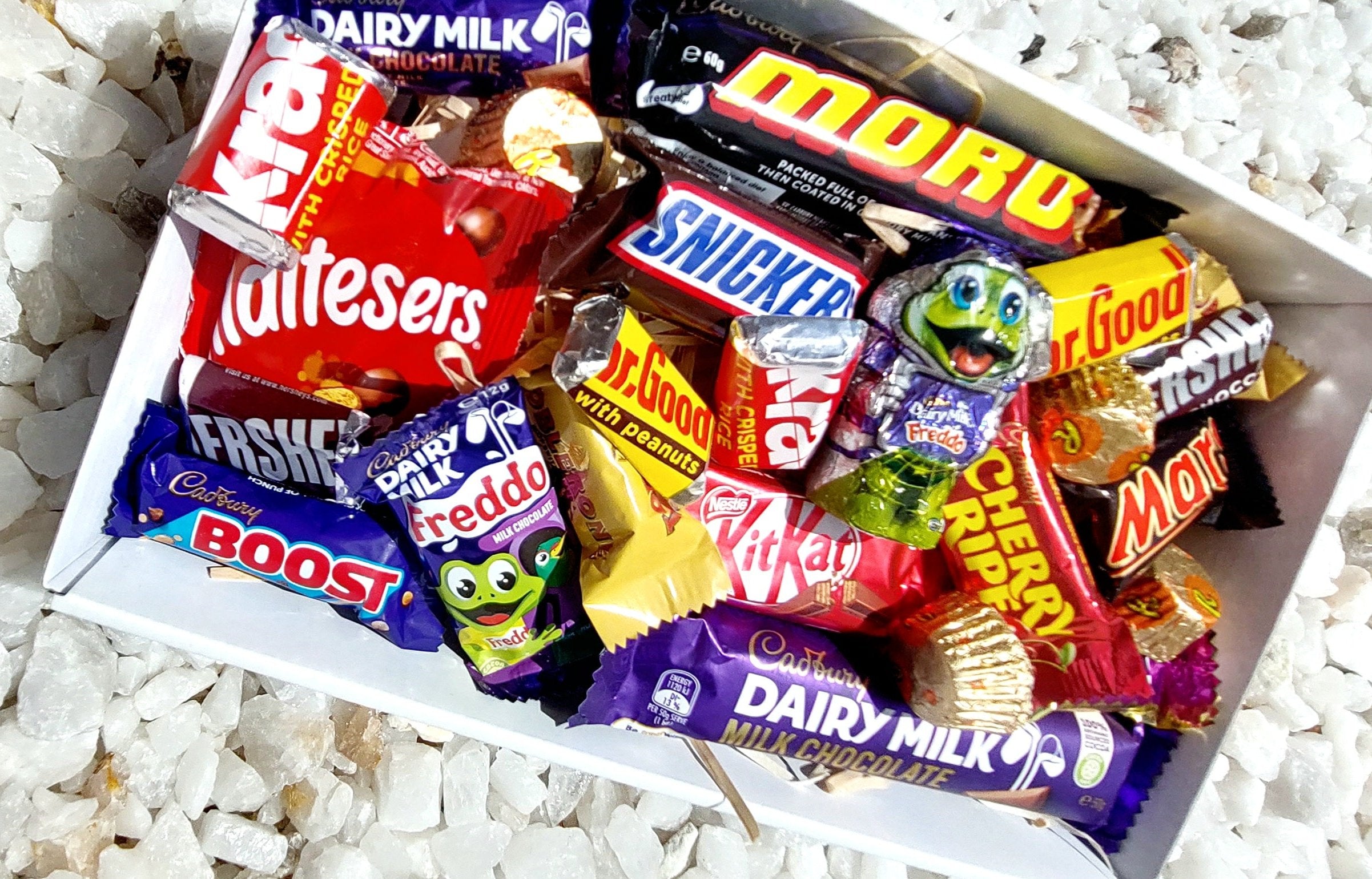 Chocolate Extravaganza Gift Box: A delightful treat for any chocolate lover, filled with a Candy-filled Freddo, Freddo Frog, 8 Mini Hershey's bars, assorted mini chocolates, full-sized Cadbury Milk and Moro bars, all beautifully gift-boxed and topped with lollies and exclusive confetti. Perfect for gifting or self-indulgence!