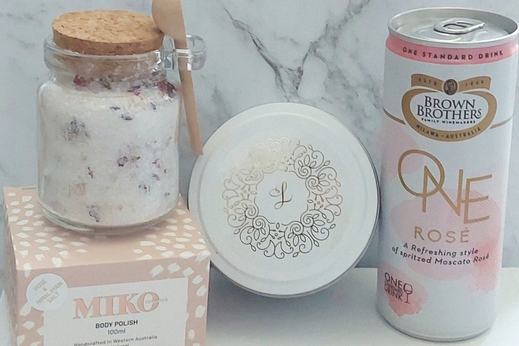Personal Indulgence Gift Box: Perfect for relaxation with Brown Brothers One Moscato Rosé, bath salts, Lenx Natural Soy Candle (WA Made), Miko Cosmetics Body Polish (Rose & Himalayan Salt), and Hershey's Kisses. Finished with signature confetti for a blissful and luxurious experience.